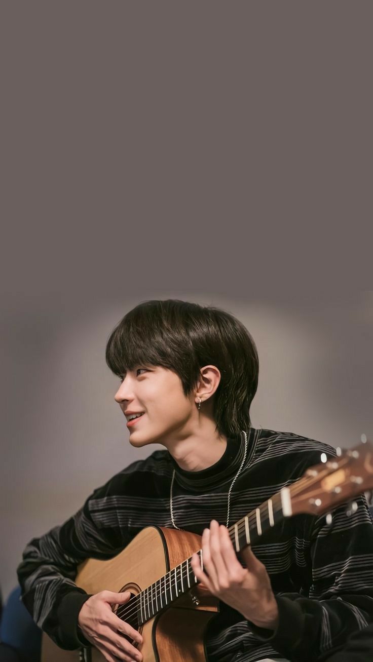 a young man playing an acoustic guitar while wearing headphones