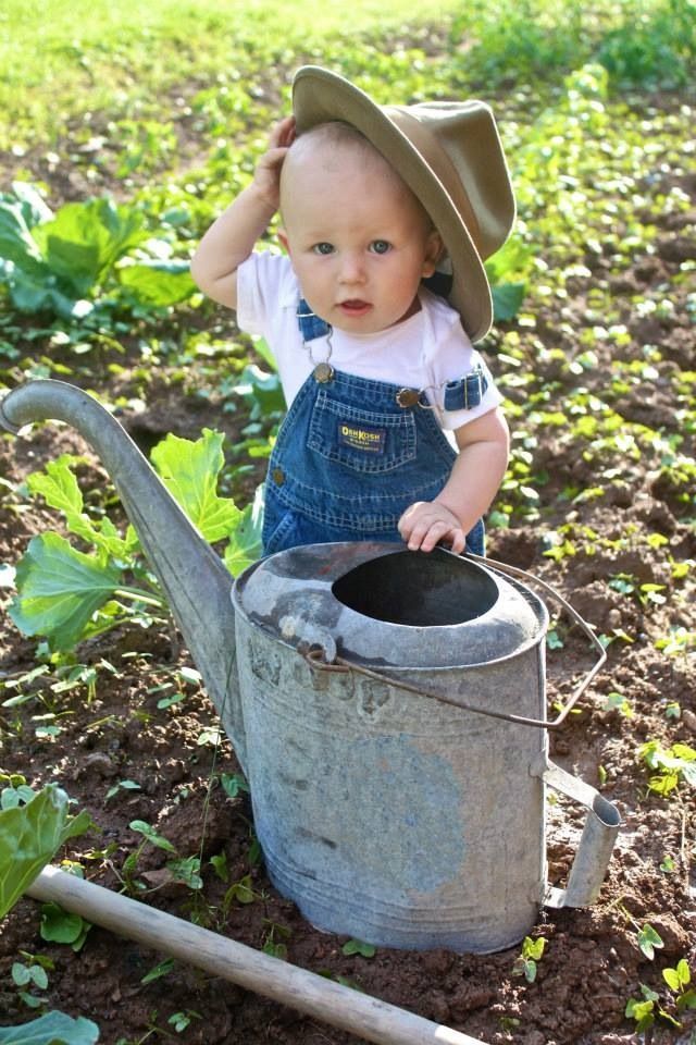 a small child wearing overalls and a hat is holding a watering can in the dirt