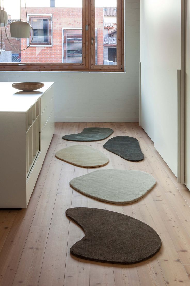 four rugs are arranged on the floor in front of an open window, near a sink