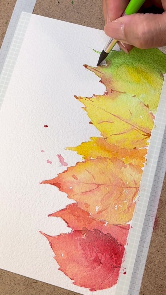 a person is using a pencil to paint leaves on paper with colored watercolors