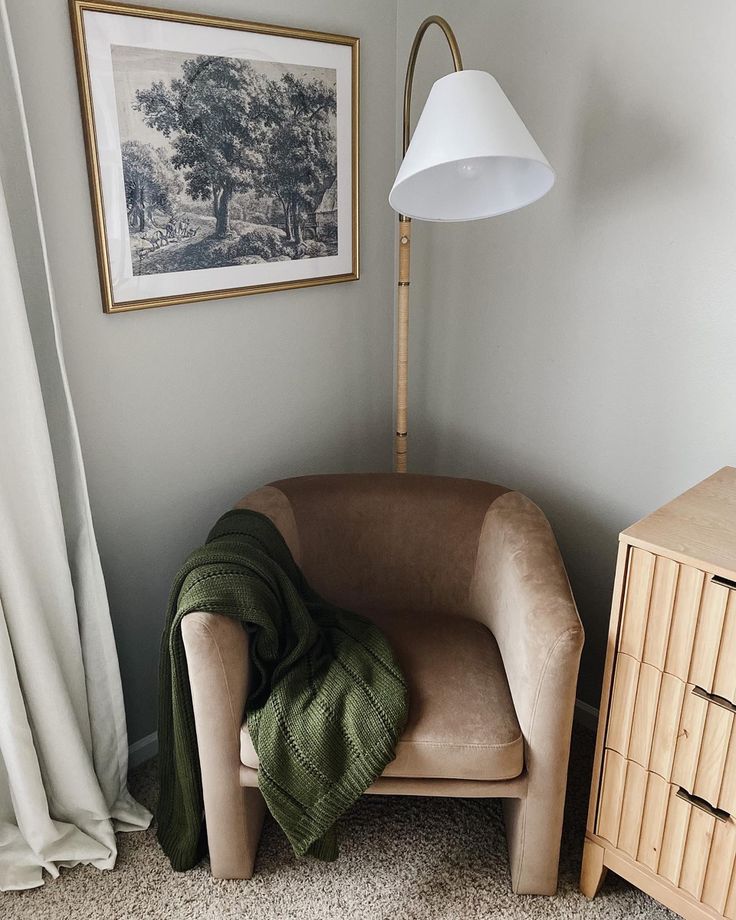 a chair with a blanket on it in front of a lamp and pictures hanging on the wall