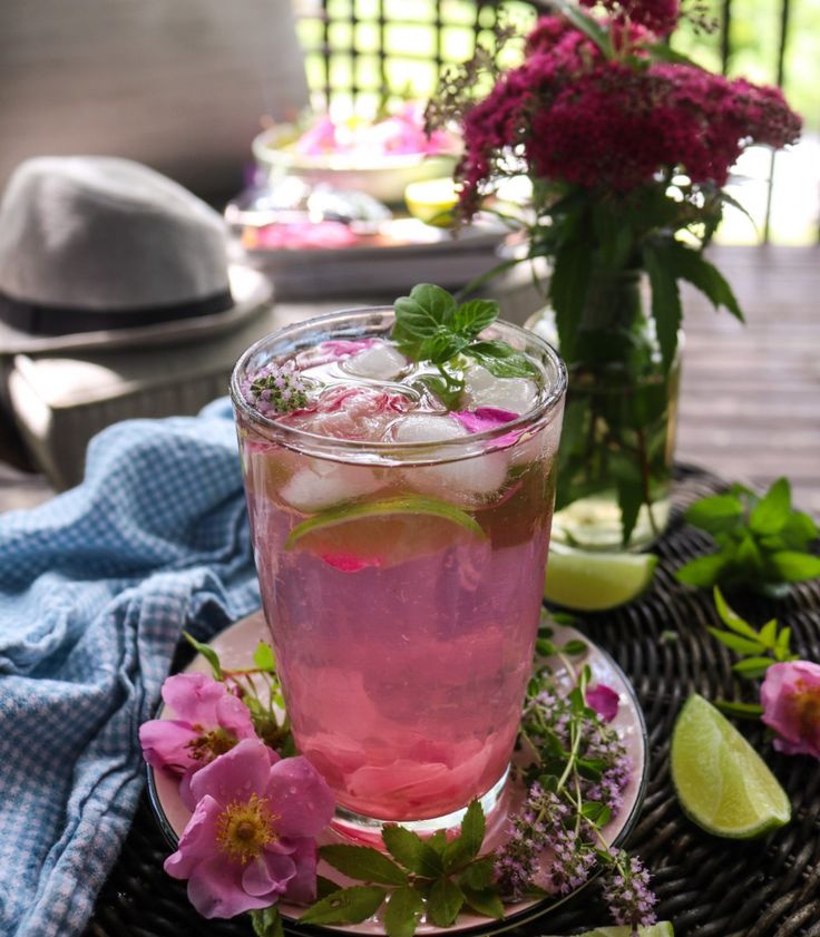 a glass filled with pink liquid sitting on top of a table next to flowers and limes