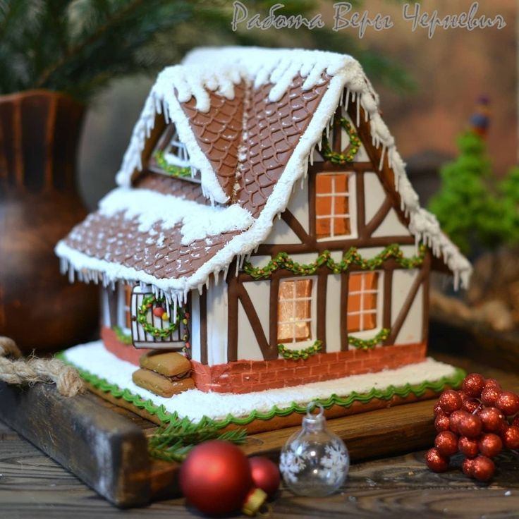 a gingerbread house decorated with icing and christmas decorations on a wooden table next to ornaments