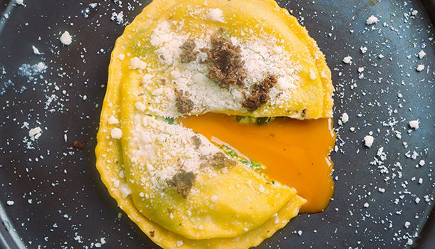 an omelet with cheese and other toppings sits on a black plate covered in powdered sugar