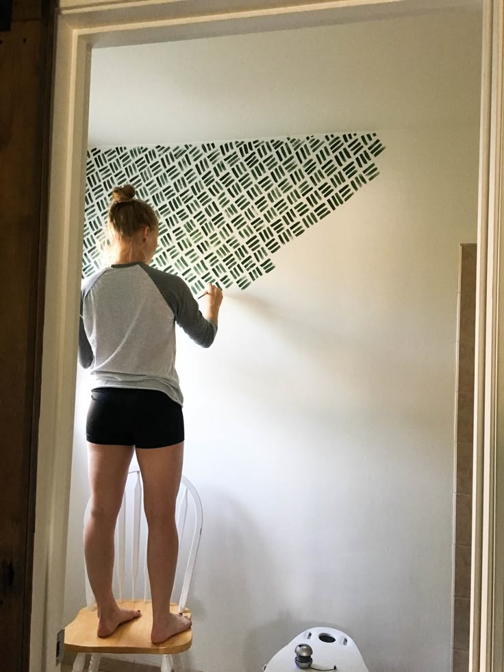 a woman standing on top of a chair painting a wall