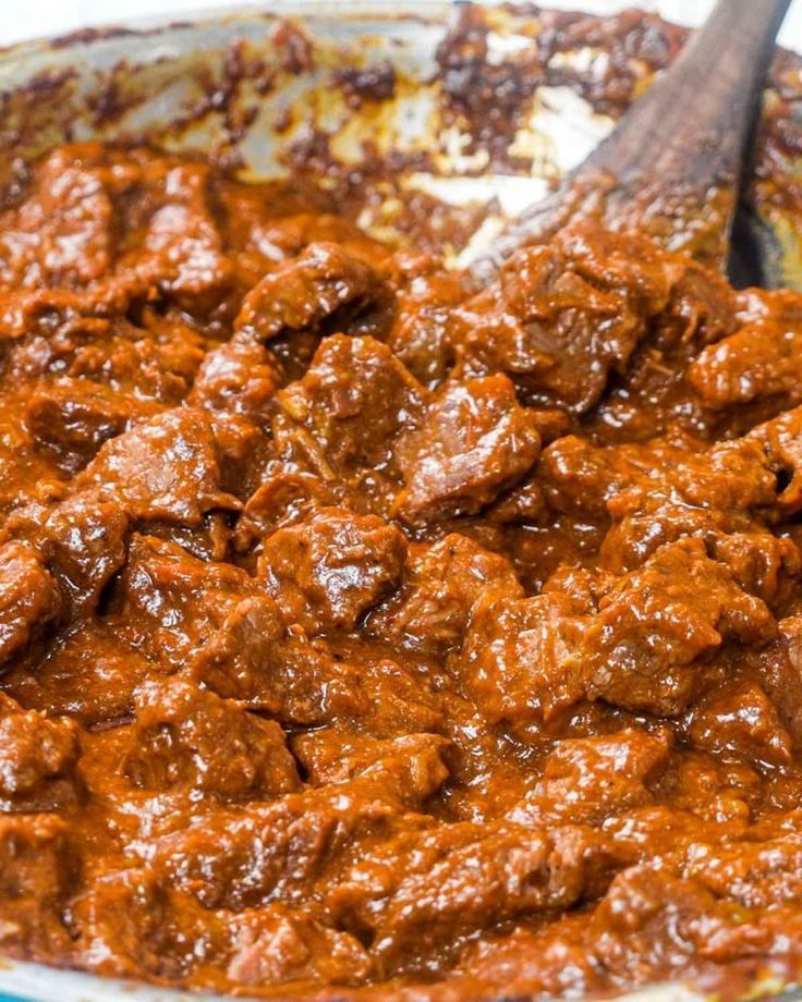 a large pot filled with meat on top of a wooden spoon and sauce in it