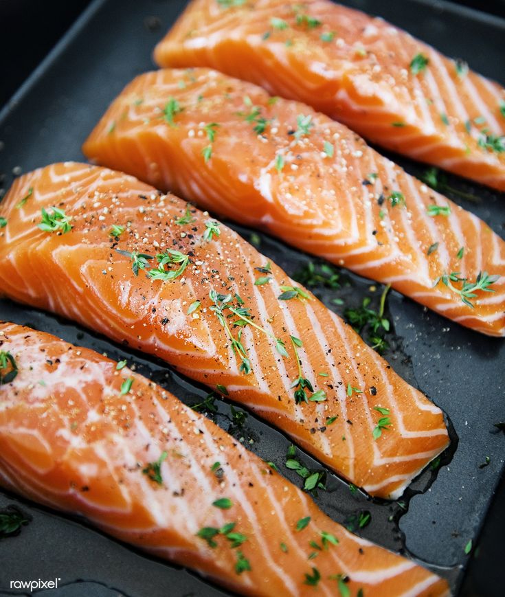 four raw salmon fillets in a pan with seasoning sprinkled on top