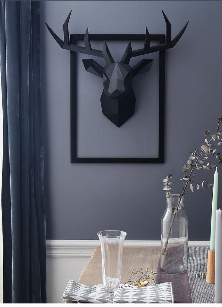 a deer head mounted on the wall above a table with two glasses and vases