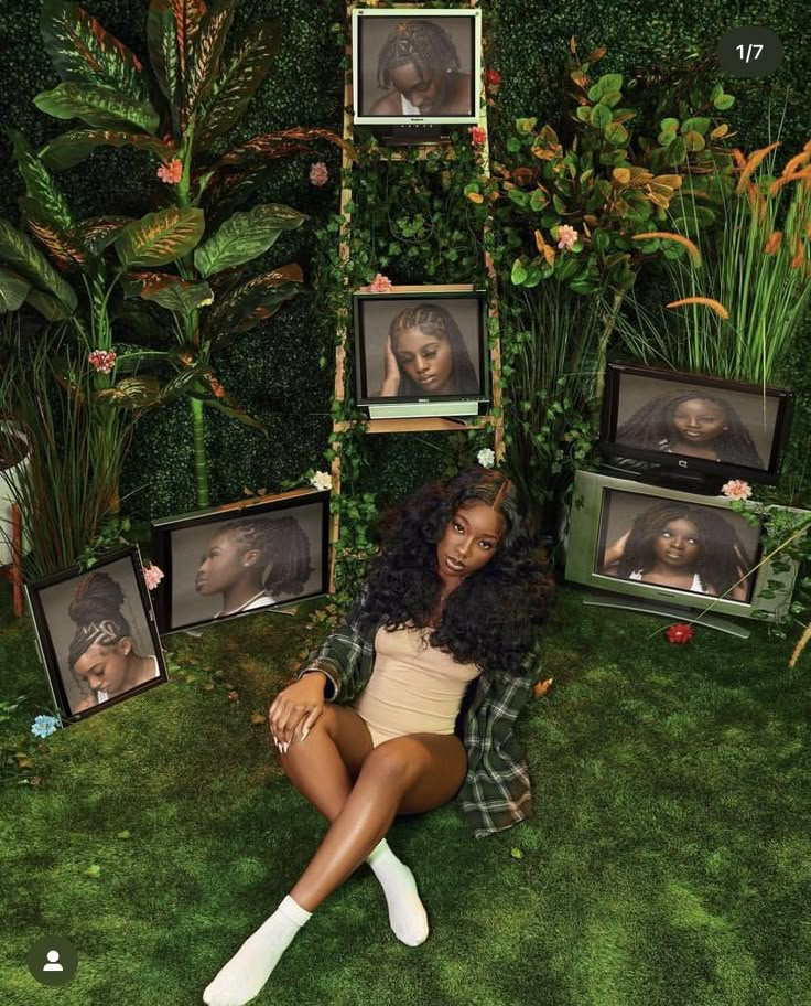 a woman sitting on the ground in front of some framed pictures and flowers with her legs crossed