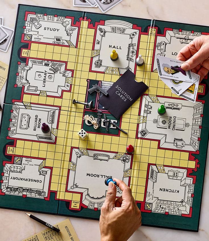 two hands playing monopoly on a board game set up with pieces of paper and dice