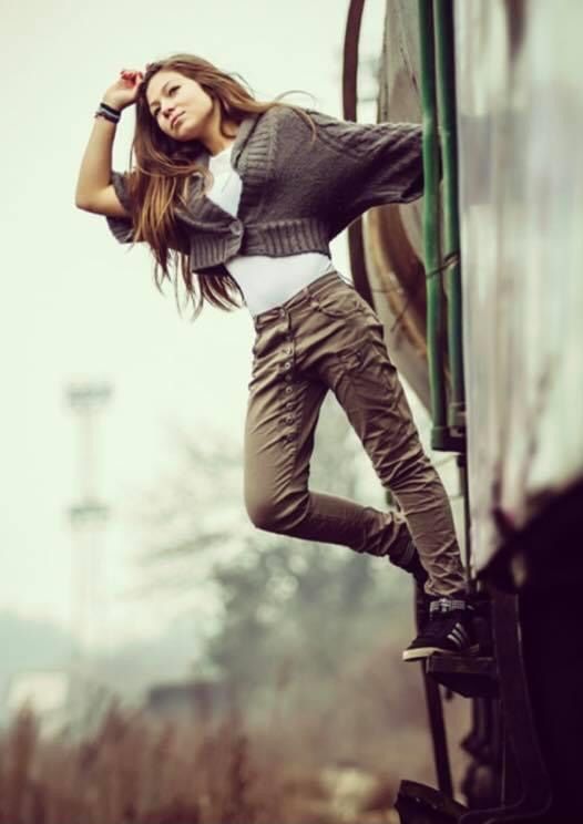 a woman leaning on the side of a train while wearing brown pants and a sweater