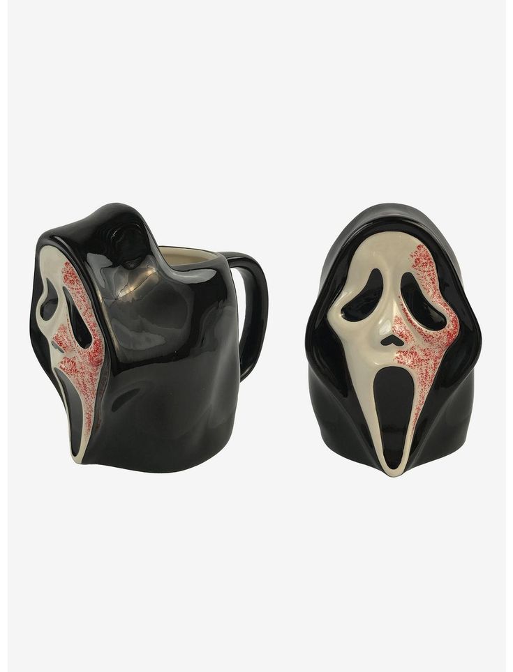 two black and white ceramic mugs with red designs on the sides, one is shaped like a mask