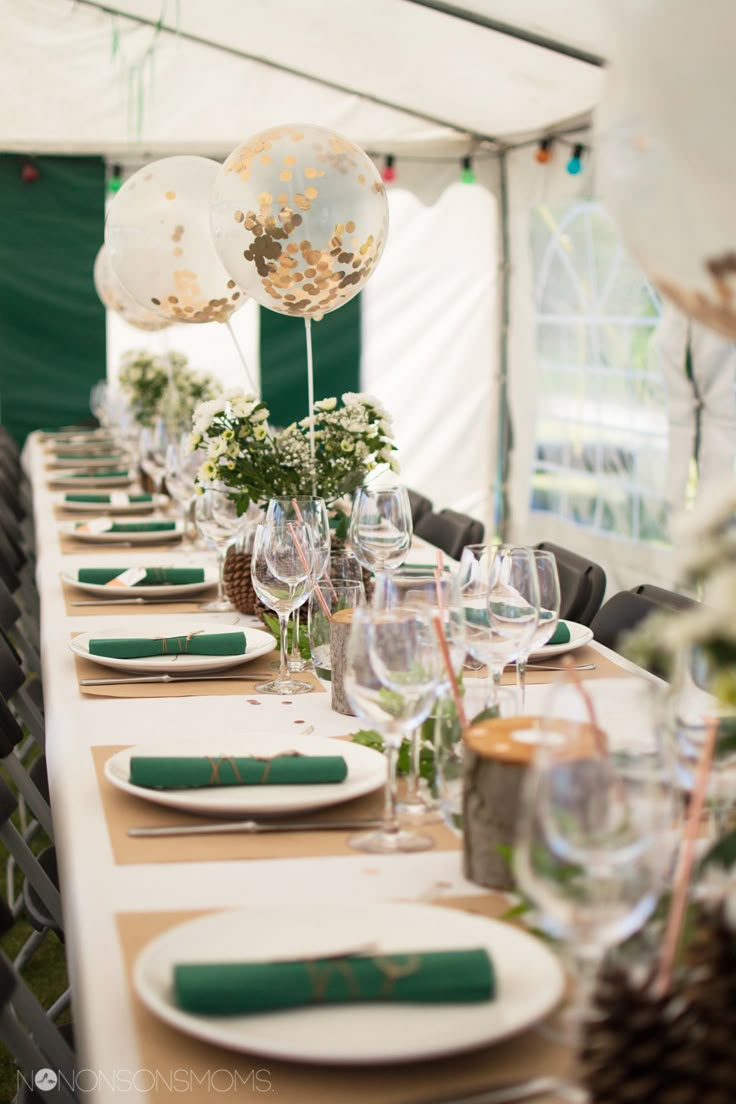 the table is set with plates, glasses and balloons