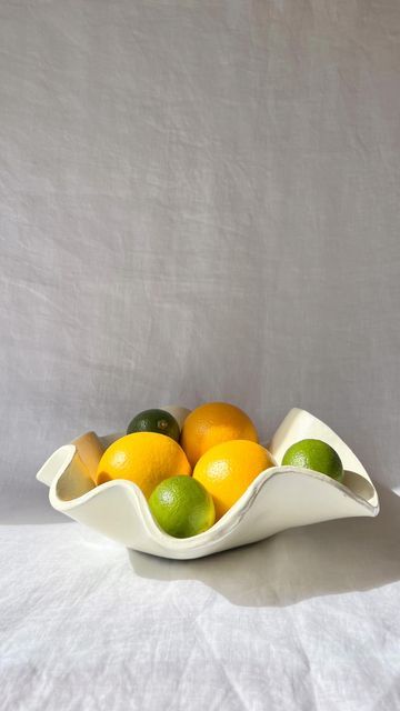 a bowl filled with lemons, limes and oranges on a white surface