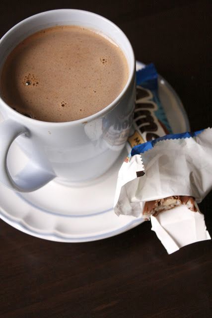 a cup of coffee and some candy bar wrappers on a saucer with a spoon