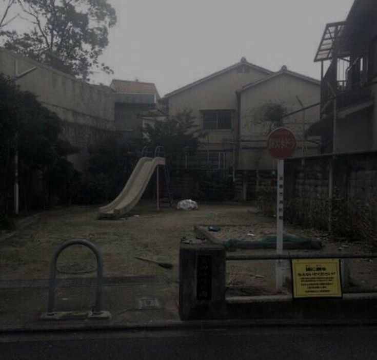 an empty yard with a slide in the middle and houses behind it on a foggy day