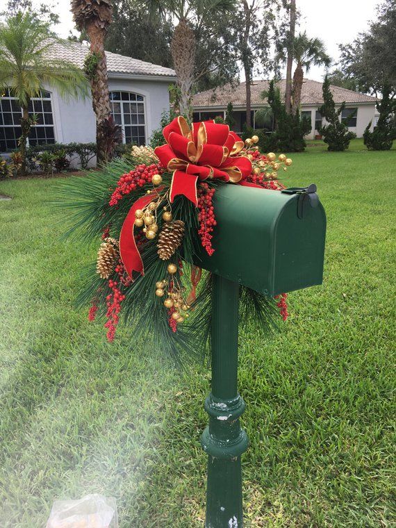 a green mailbox decorated with red and gold christmas decorations, pine cones and bows