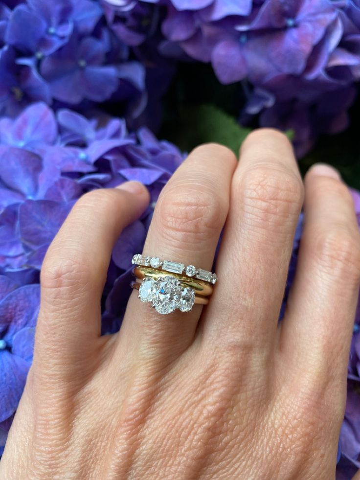 a woman's hand with two rings on it and purple flowers in the background