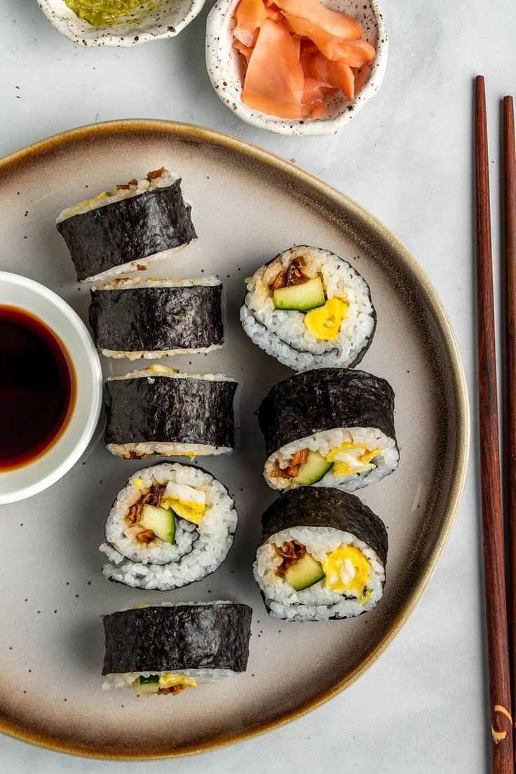 sushi on a plate with chopsticks next to it and sauce in a bowl