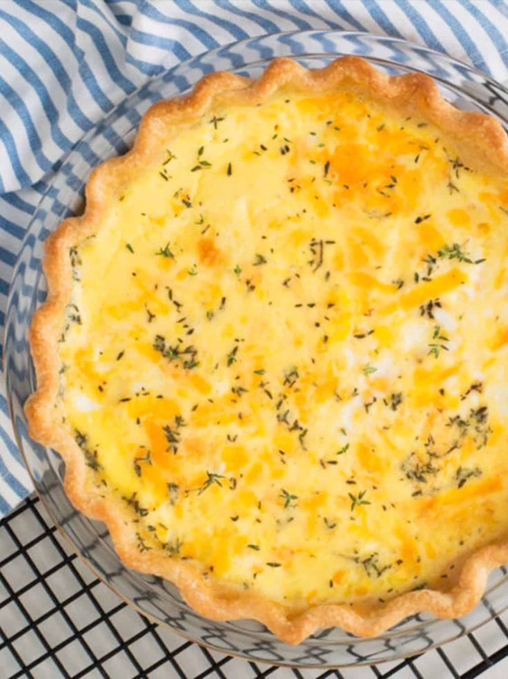 a quiche with cheese and herbs in a glass pie dish on a wire rack