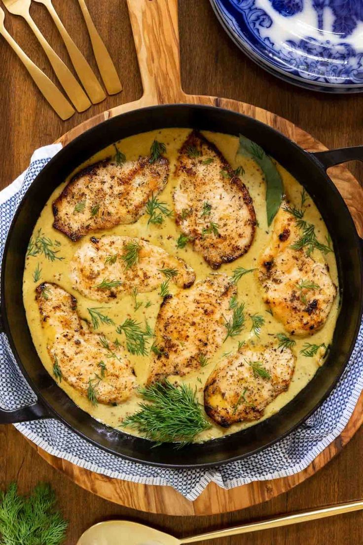 a skillet filled with chicken and cheese on top of a wooden table next to utensils