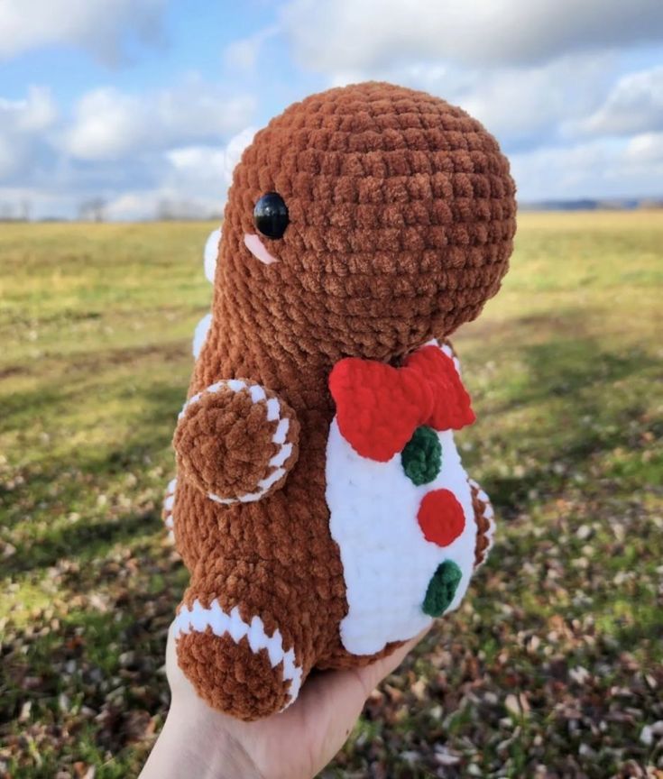 a hand holding a brown crocheted stuffed animal with a red bow on its neck