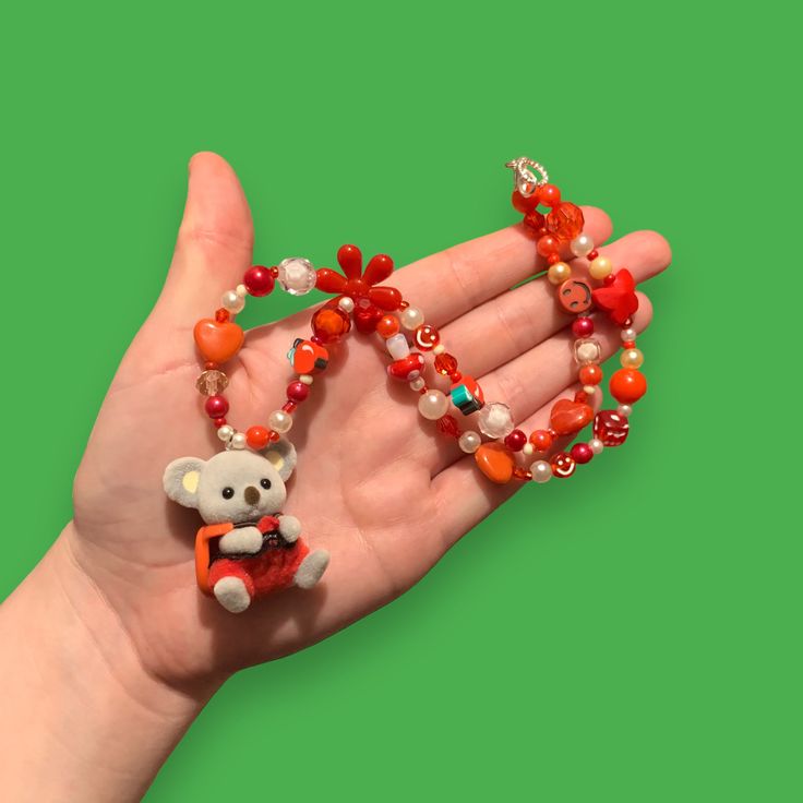 a person's hand holding an orange and white beaded necklace with a monkey on it