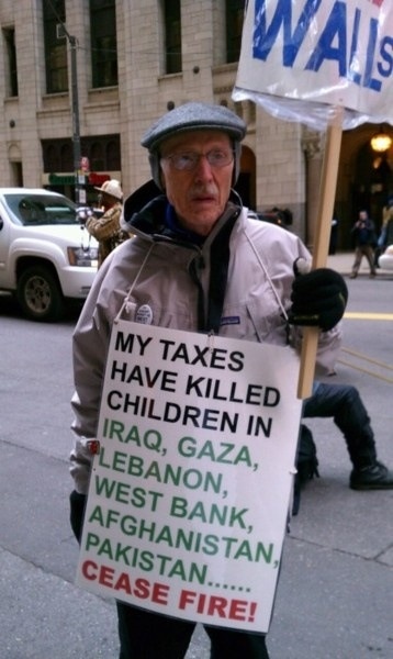 a man holding a sign that says my taxes have killed children in iraq, lebanon, west bank, pakistan, case fire