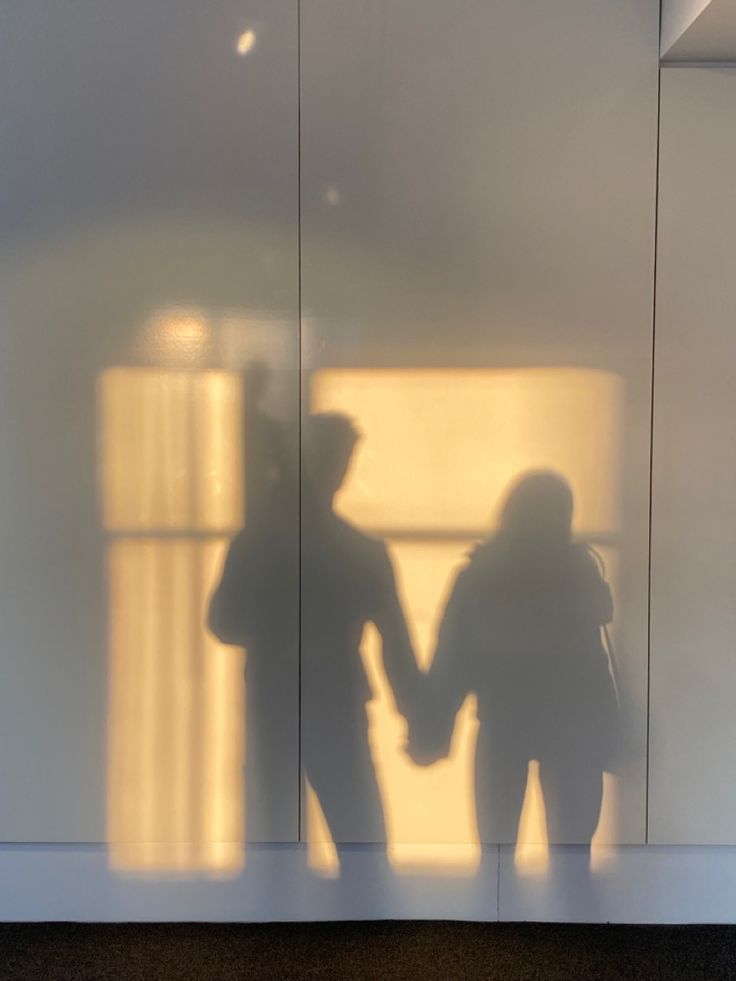 the shadow of two people holding hands in front of a glass wall with sunlight coming through it