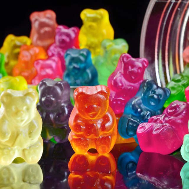 a jar filled with gummy bears sitting on top of a black table next to a pile of other gummy bears