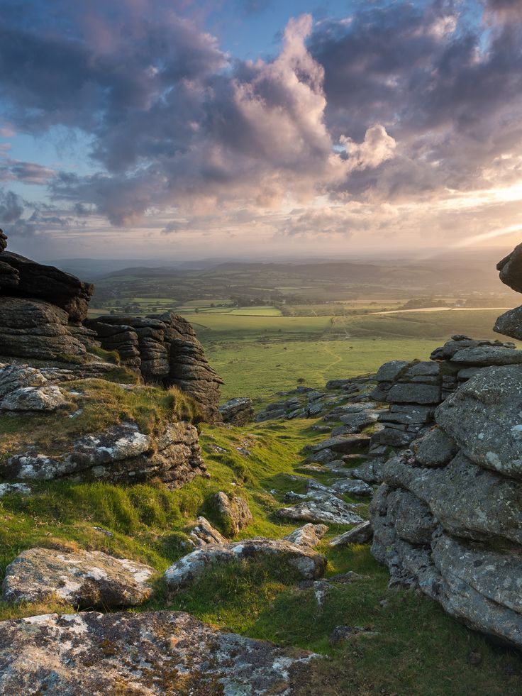 the sun is setting over some rocks and green grass in the foreground, with clouds overhead