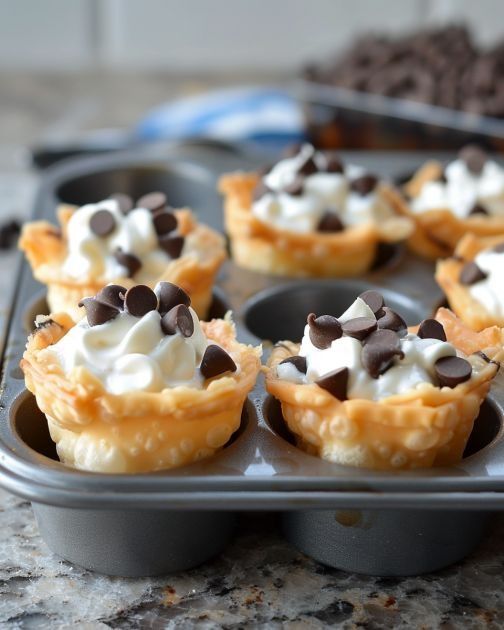 mini cupcakes with chocolate chips and whipped cream in a muffin tin on a counter