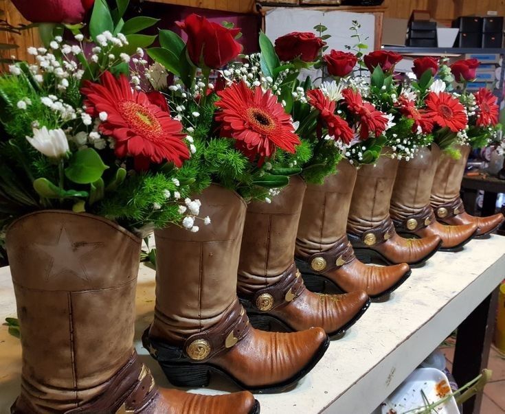 many boots with flowers in them are lined up on a table and ready to be used as vases