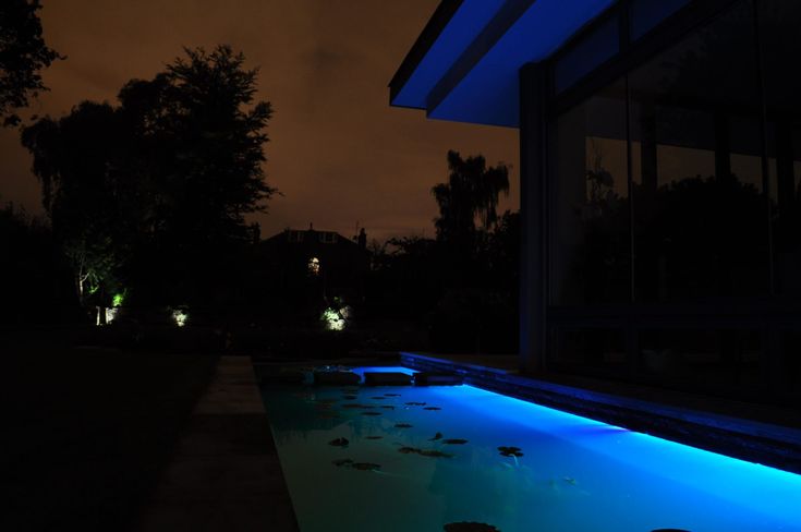 an outdoor pool lit up at night with blue lights on the water and trees in the background