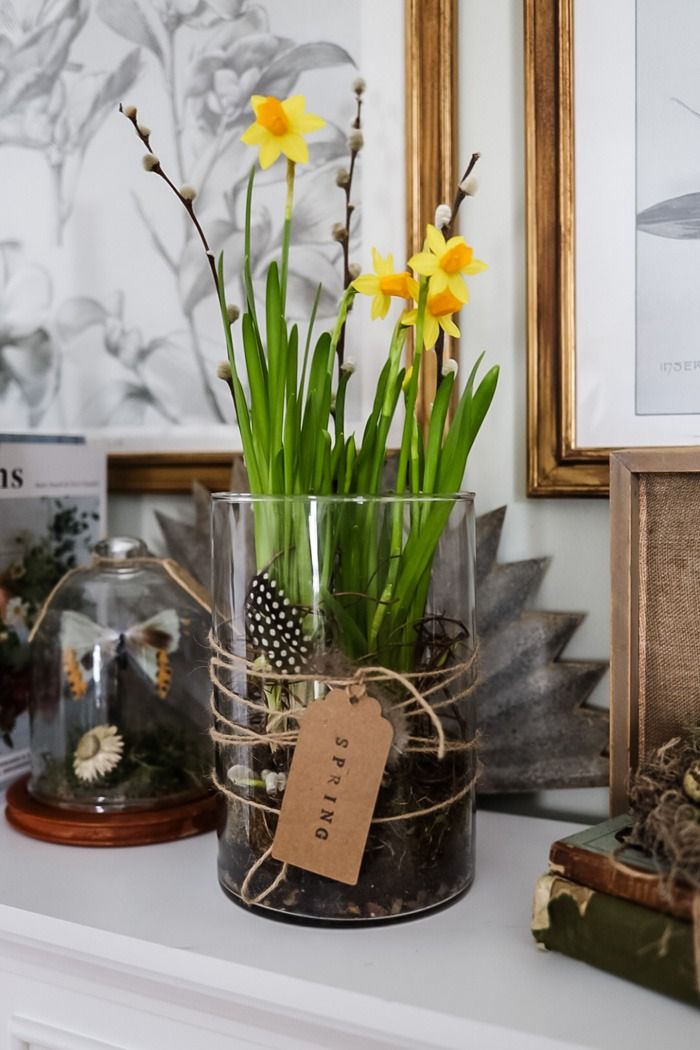 some flowers are in a glass vase on a mantle with other items and pictures behind it