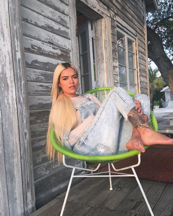 a woman sitting in a green chair on a porch with her legs crossed, looking at the camera