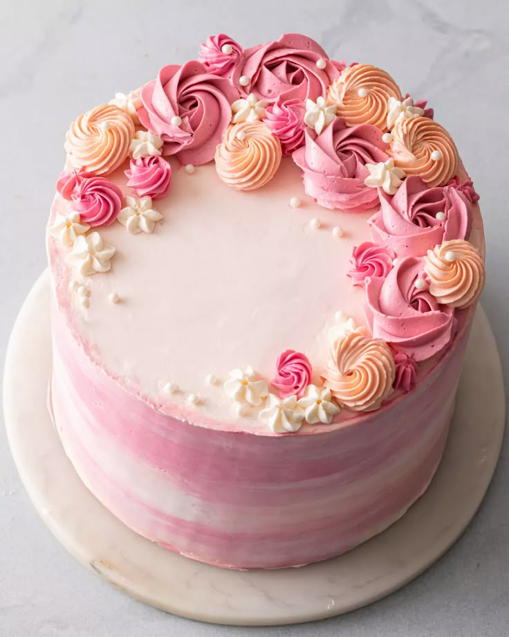 a cake with pink frosting and flowers on top is sitting on a white plate