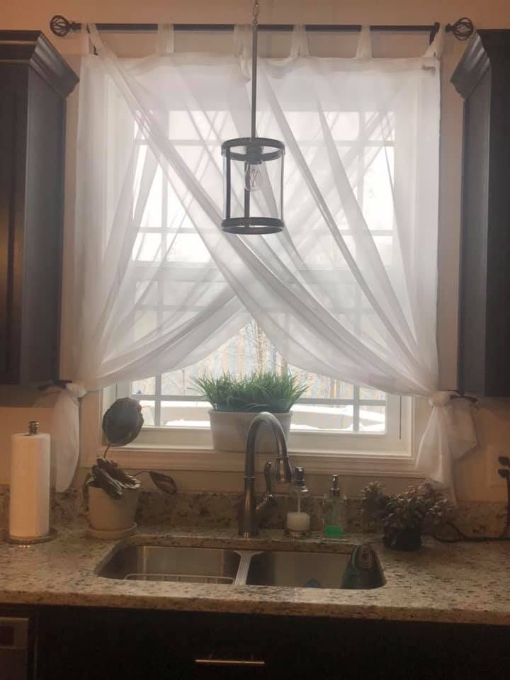 a kitchen sink under a window covered in white curtains