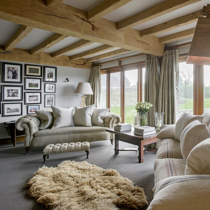 a living room filled with furniture and windows covered in wood beams on the ceiling