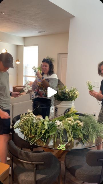 three people standing around a table filled with plants