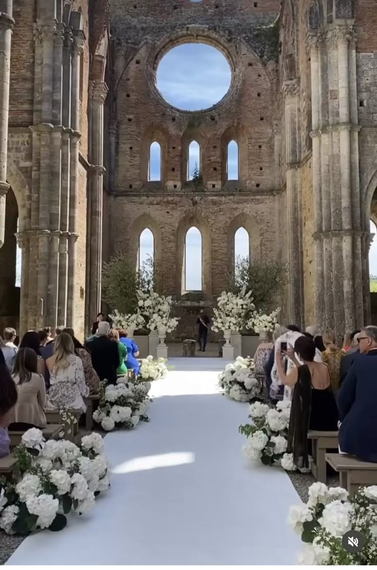 a wedding ceremony in an old building with white flowers and greenery on the aisle