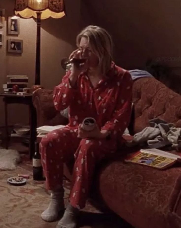 a woman in red pajamas sitting on a couch drinking from a cup and talking on the phone