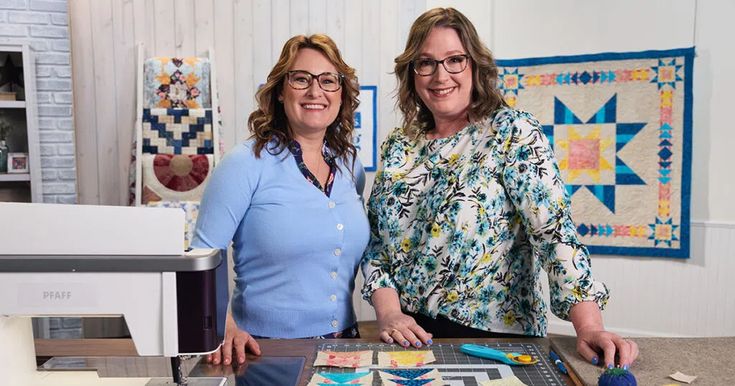 two women standing next to each other in front of a table with quilts on it