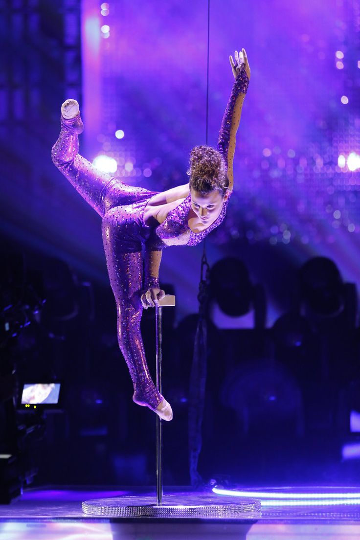 a woman is performing on a pole in the middle of a dance performance with purple lights behind her