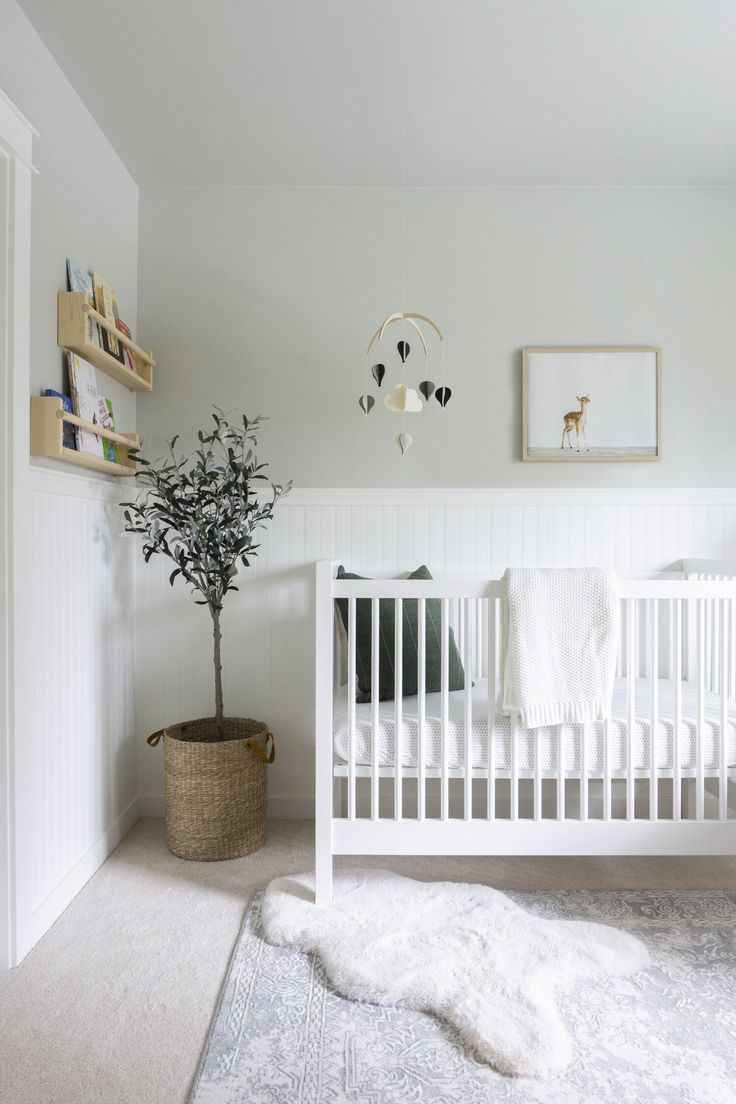 a white crib with a tree in the corner and rug on the floor next to it