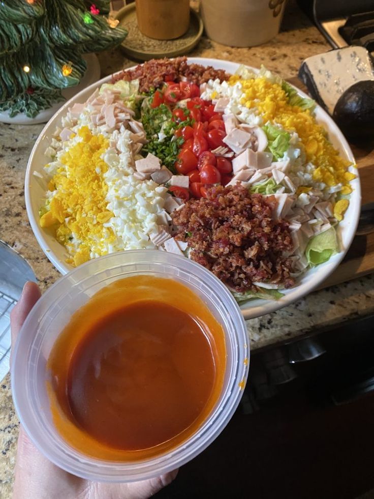 a person holding a plastic bowl filled with salad and sauce on top of a counter