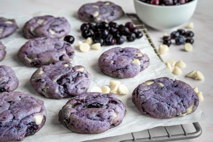 blueberry cookies and white chocolate chips are on a baking sheet next to a bowl of cherries