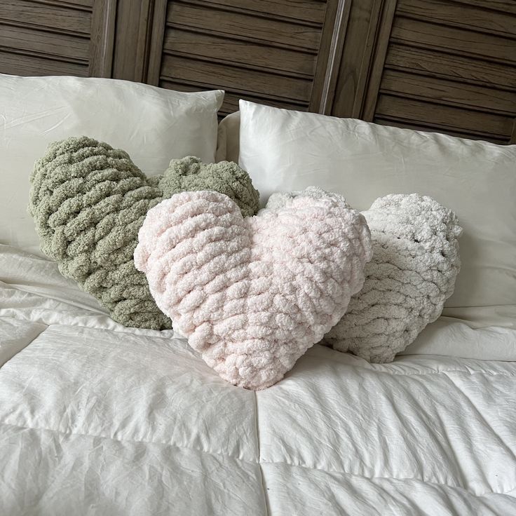 three knitted heart pillows sitting on top of a bed