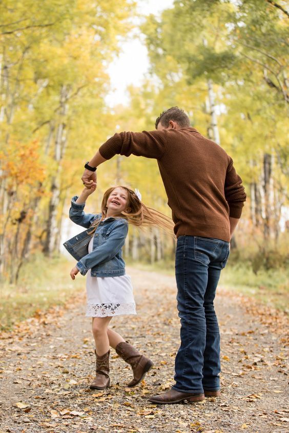 a man and woman walking down a dirt road in the woods with leaves on the ground