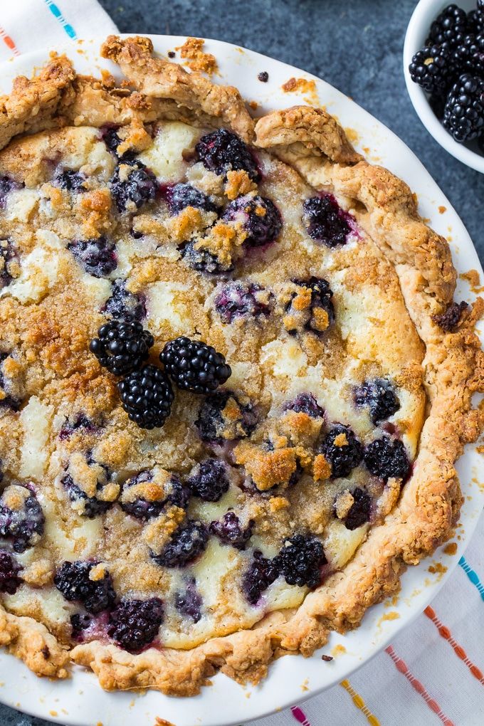 blackberry cream pie on a white plate with blueberries and blackberries in the background